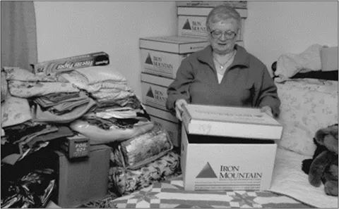 Black-and-white photo of older woman unpacking a box in bedroom.